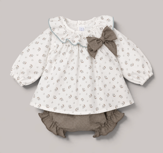 Conjunto NAVIA para bebé niña con blusa blanca floral, cuello volante, lazo marrón y braguita a juego con volantes.