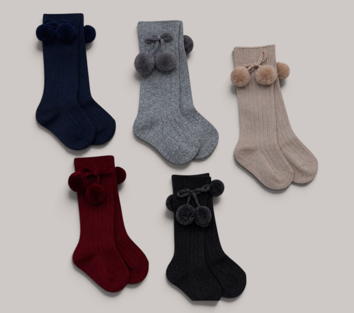 Calcetines altos NAVIA para bebé en tejido de canalé con pompones decorativos, disponibles en varios colores.