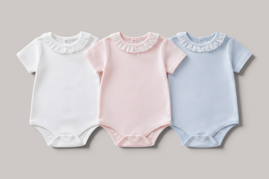Pack de tres bodies NAVIA para bebé en algodón premium, colores blanco, rosa y azul con cuello de encaje delicado.